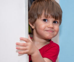 Cheeky toddler boy behind door - feature