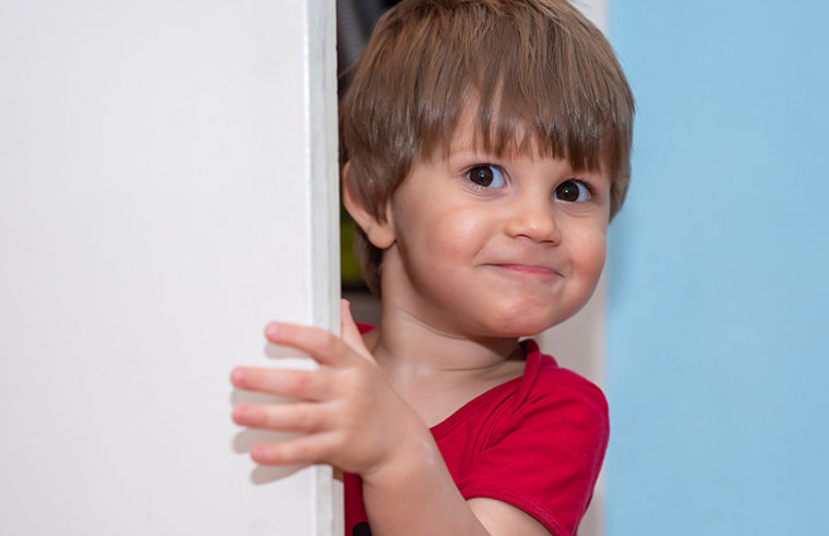 Cheeky toddler boy behind door - feature