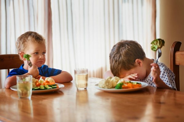 two boys eating dinner with vegetables