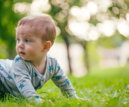Baby crawling on grass in onesie - feature