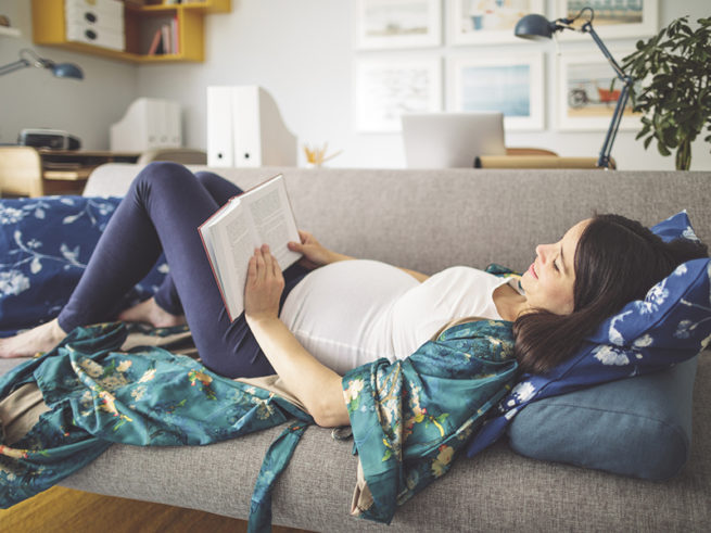 Pregnant woman lying on couch reading book