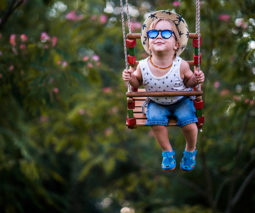 Toddler boy with sunglasses and hat on swing - feature