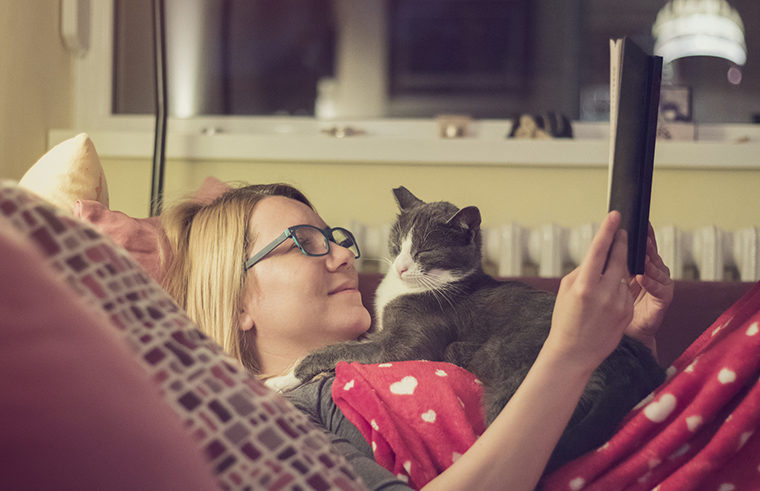 Woman reading book on couch with cat - feature