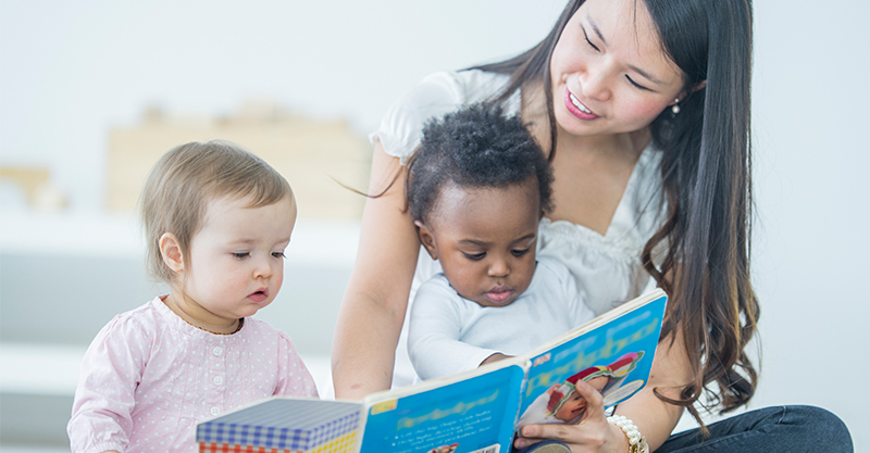 Two toddlers being read to by young woman