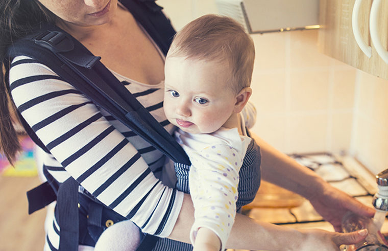 Mother babywearing baby in carrier while at the sink