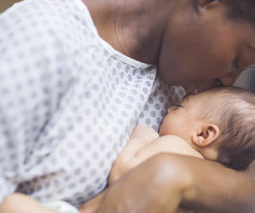 Mother in hospital gown kissing newborn baby - feature