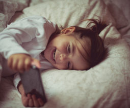 Toddler lying down with iphone smiling - feature