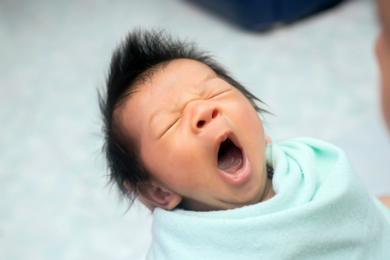 tired newborn asian baby yawning
