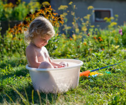 Child sitting in bucket of water in garden - feature