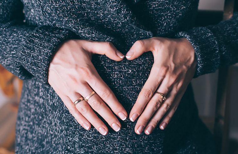 Pregnant woman wearing jumper with heart hands - feature