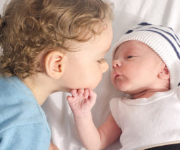 toddler kissing newborn sibling - feature