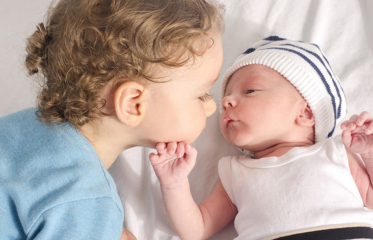 toddler kissing newborn sibling - feature