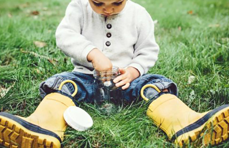 Child sitting in grass with gumboots and glass jar - feature
