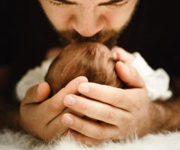 Father holding newborn head and kissing baby - feature