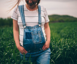 Happy pregnant woman in overalls walking in field - feature