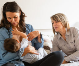 Mother breastfeeding baby on bed with grandmother looking on