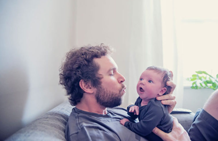 Father holding awake newborn on couch - feature