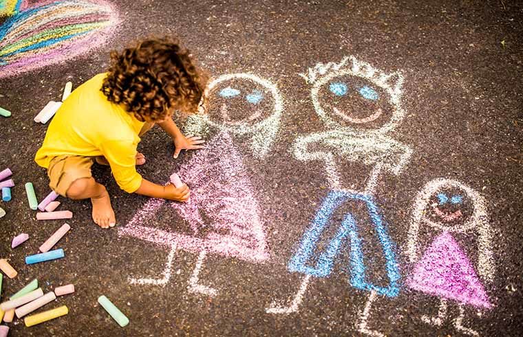 Young boy drawing with chalk on footpath - feature