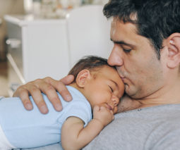 Father with newborn baby on chest kissing head - feature