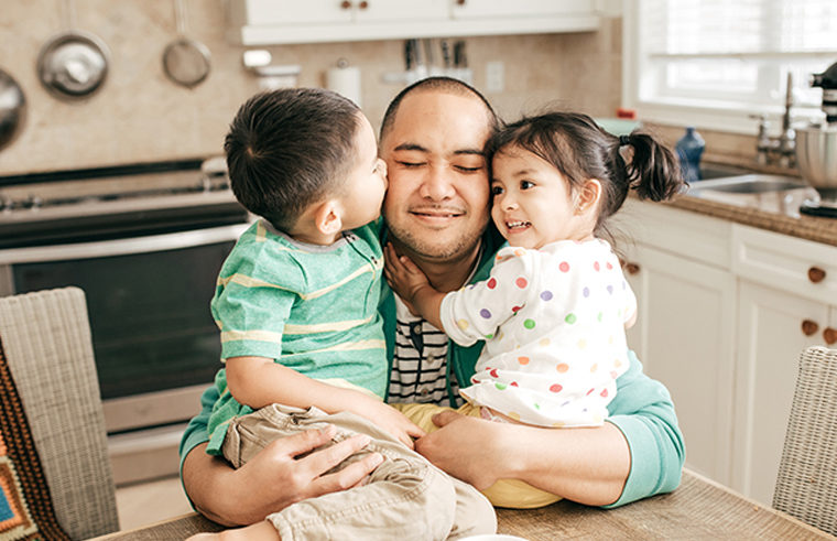 Asian dad cuddling two children on a table - feature