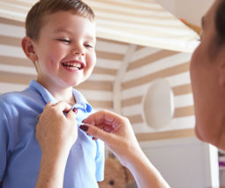 School boy getting dressed with mother - feature