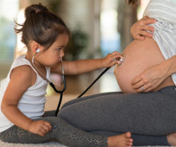 Toddler using stethoscope to listen to pregnant belly - feature