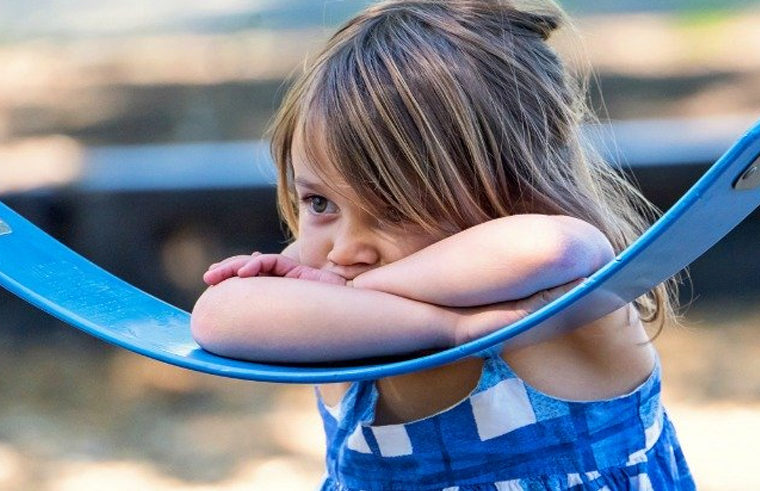 Preschool aged girl leaning on swingset looking sad