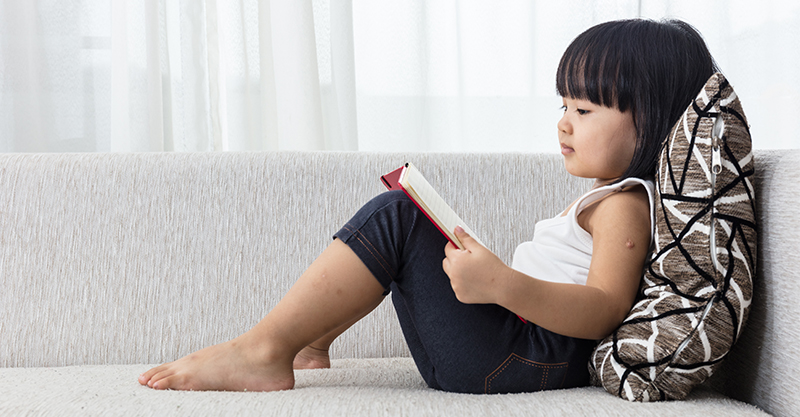Little girl on couch reading a book