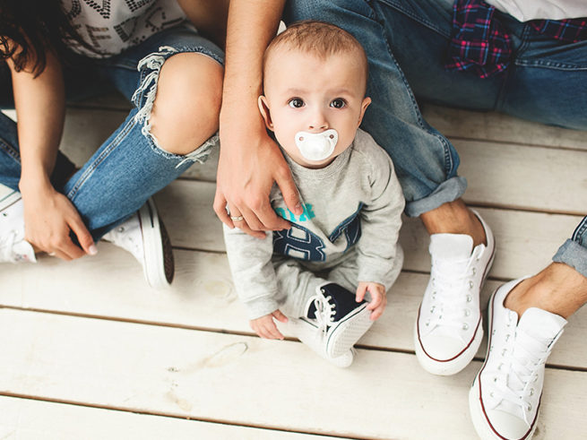 Baby with dummy sitting on floor between parents