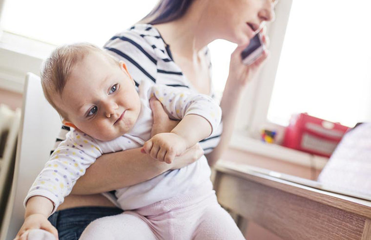 Mother on mobile phone holding baby - feature