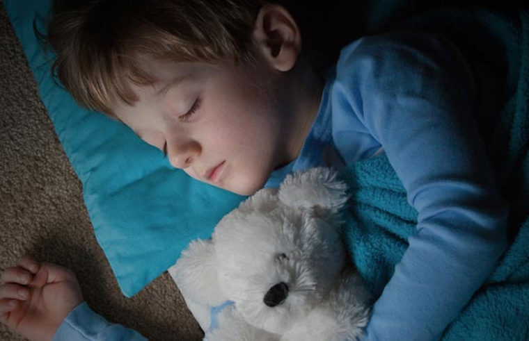 Older child asleep in bed with teddy bear
