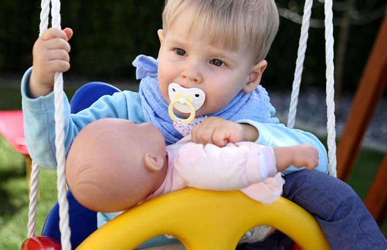 Toddler boy in swing with dummy and doll