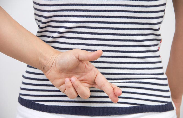 Person with stripy shirt crossing fingers behind their back - feature
