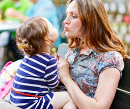 Toddler girl sitting in mum's lap with a lollipop in a cafe - feature