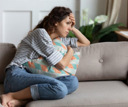 Sad woman sitting on couch hugging cushion - feature
