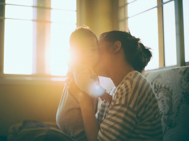 Mother kissing baby in sunlit room