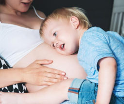Toddler lying with his ear to his pregnant mother's belly
