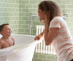 Prechool aged boy laughing in the bath with mum watching
