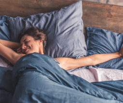Happy woman stretching out in bed alone - feature