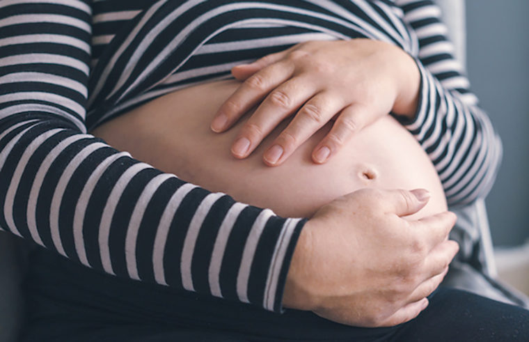 Woman in striped shirt holding pregnant belly - feature