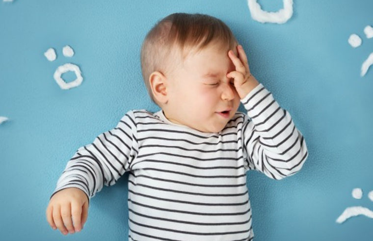 Upset baby with headache touching head- feature