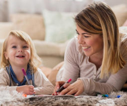 Toddler girl and babysitter lying on floor colouring in book - feature