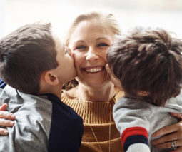 Two boys brothers kissing mother - feature