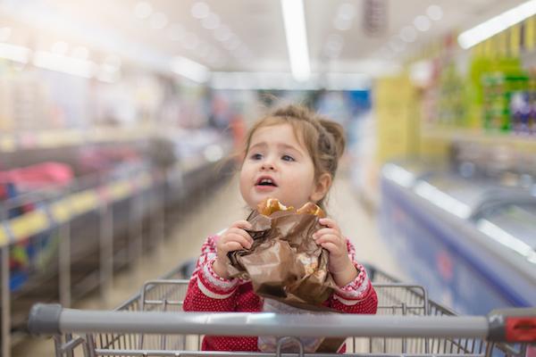 Toddler girl eating pretzel in supermarket