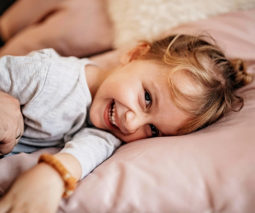 Young girl lying on bed laughing with father dad - feature