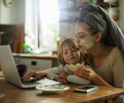 Mother with child on her lap eating and using laptop - feature