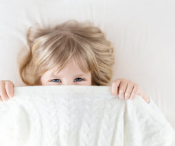 Preschool girl hiding under bed sheets - feature