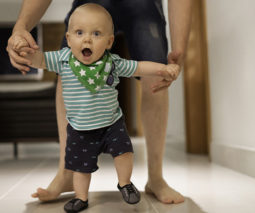 Baby boy walking holding on to father's hands - feature