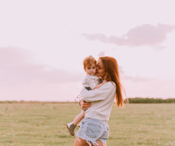 Mother hugging and holding toddler girl in field - feature