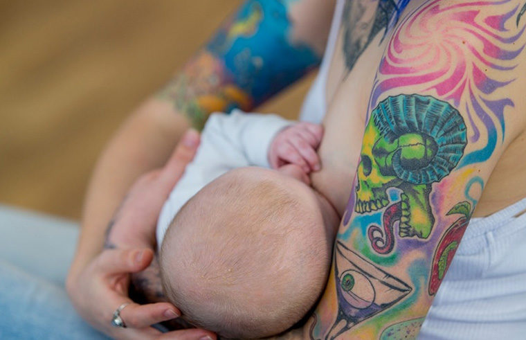 Mother with tattoos breastfeeding newborn baby